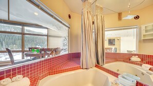 Un baño con dos tinas grandes, un ventanal con vistas a un bosque nevado y un salpicadero con azulejos rojos.