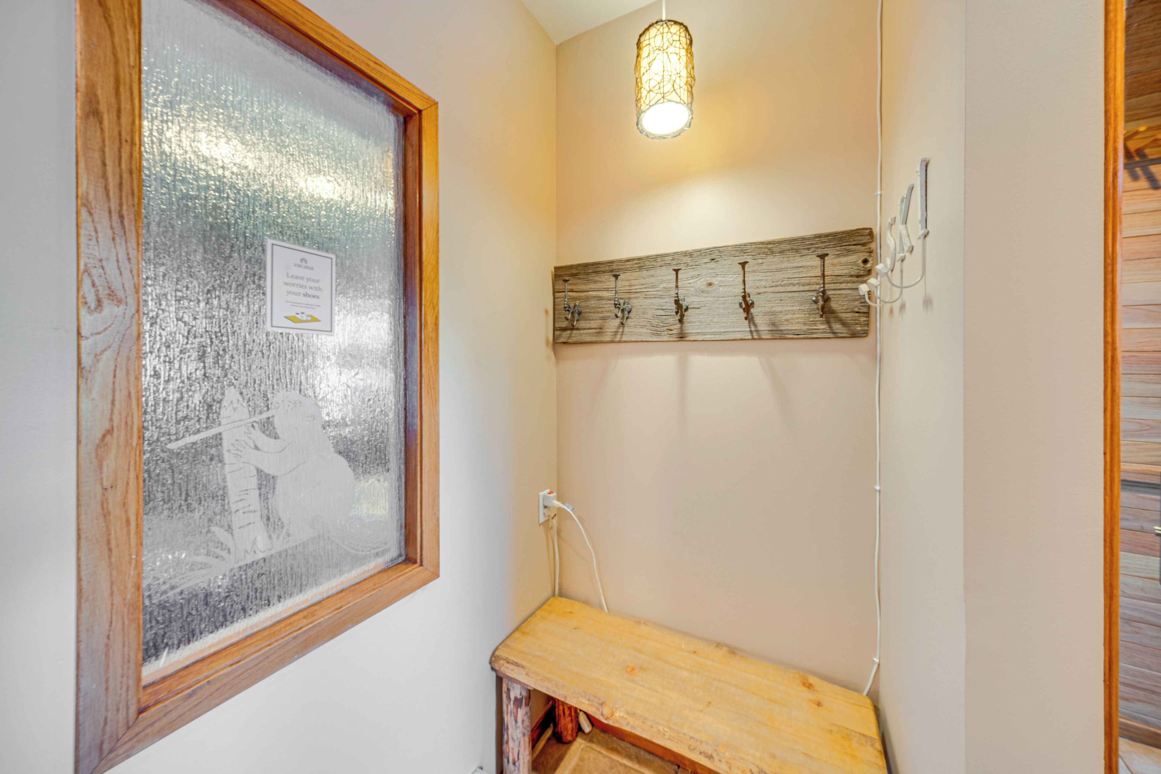 Ett badrum med ett fönster av frostat glas, en träbänk, en väggmonterad lampa och en trähylla med krokar.