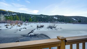 Eine Holzdielen-Terrasse mit Blick auf einen zugefrorenen See, im Hintergrund ein bewaldeter Berg.