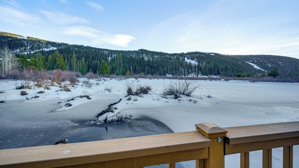 Una terraza de madera con vista a un lago congelado y una montaña boscosa al fondo.