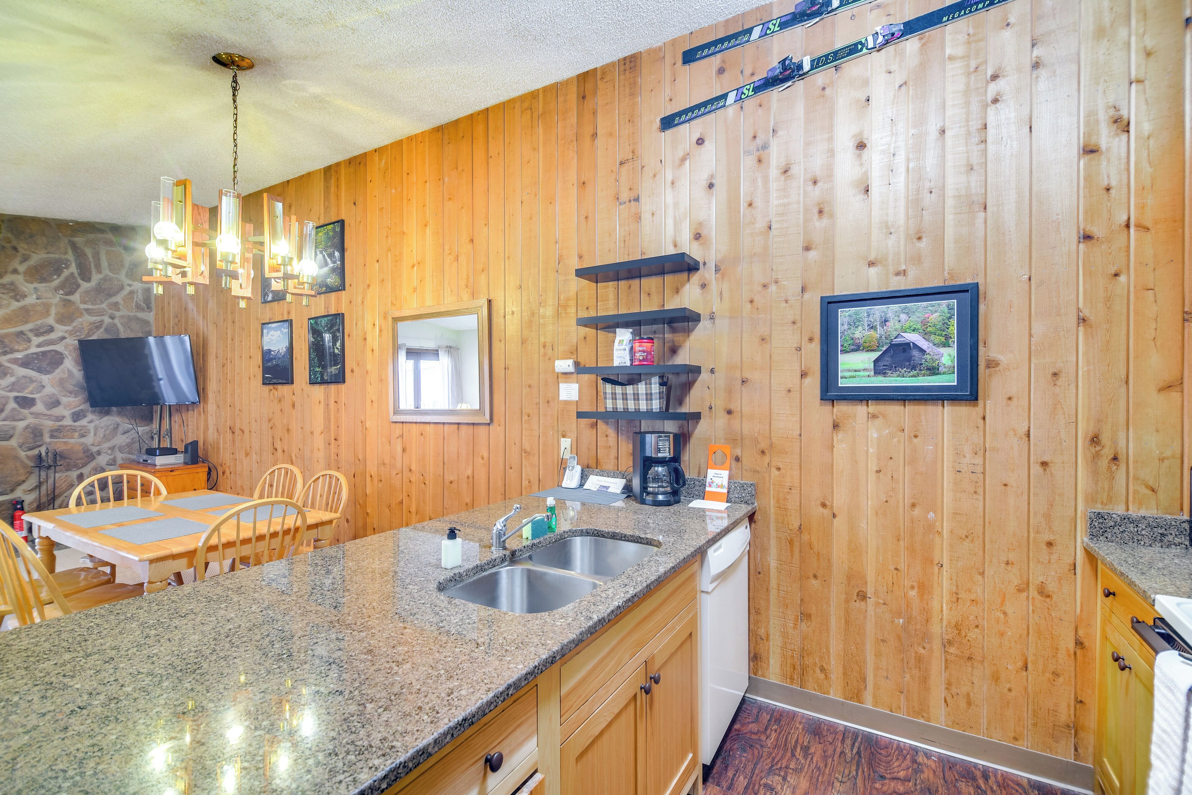 A kitchen with granite countertops, wooden cabinets, a stone wall, a wooden ceiling, and a mounted television.