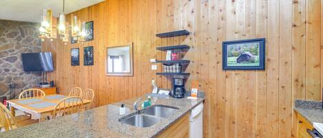 A kitchen with granite countertops, wooden cabinets, a stone wall, a wooden ceiling, and a mounted television.