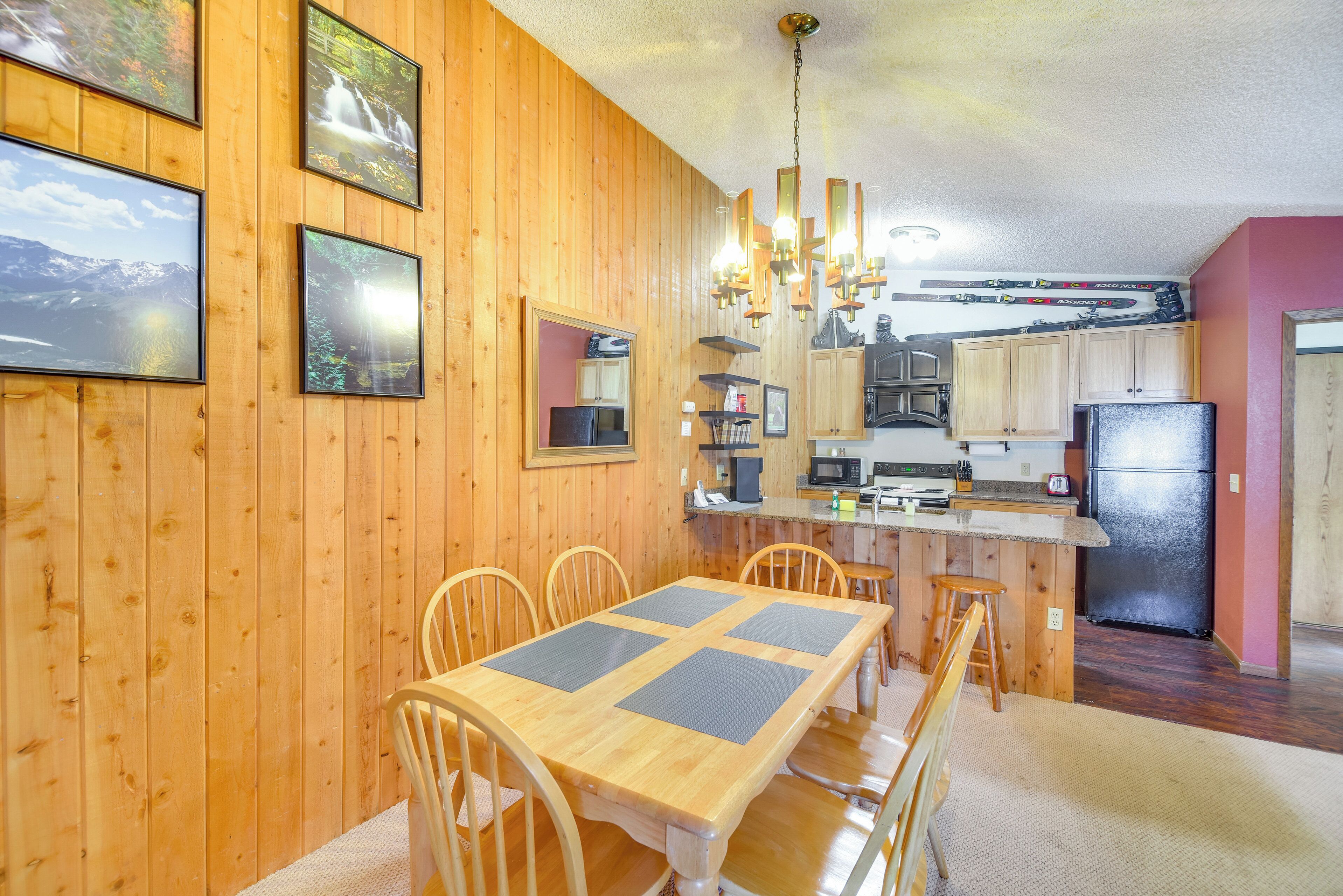 A wooden-paneled room with a dining table, chairs, a kitchen area, and a refrigerator.
