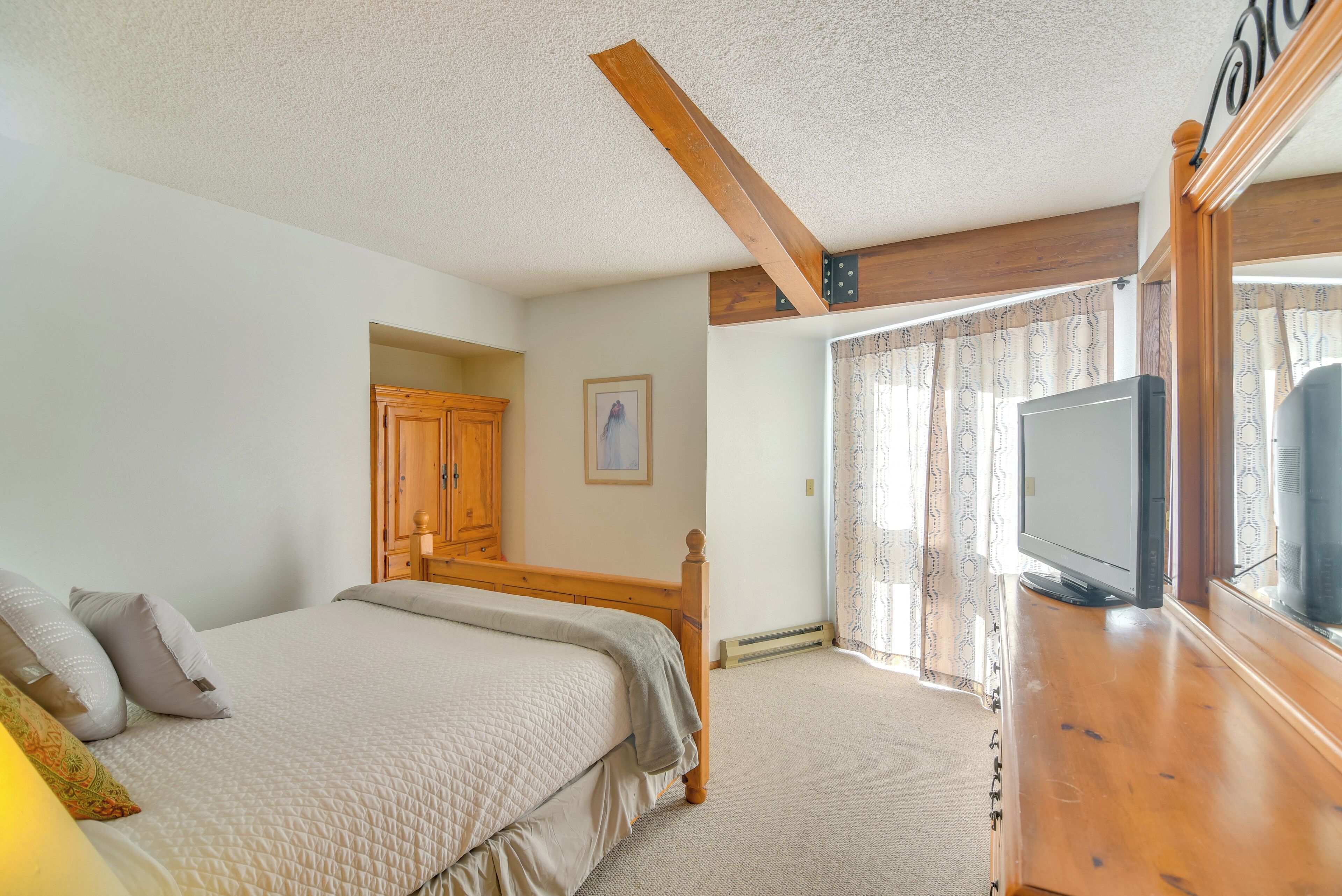 A bedroom with a bed, wooden headboard, a television, and a window with curtains.