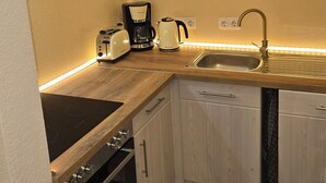 A modern kitchen with wooden cabinets, a built-in oven, a coffee maker, and a sink. - WohnTraum zur alten Post, old town, sauna (Meißen)