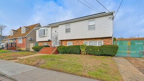 A two-story residential house with a front porch, a brick foundation, and a well-maintained lawn. - 2 Mi to UBS Arena: Wfh-friendly Couple's Retreat (Floral Park)