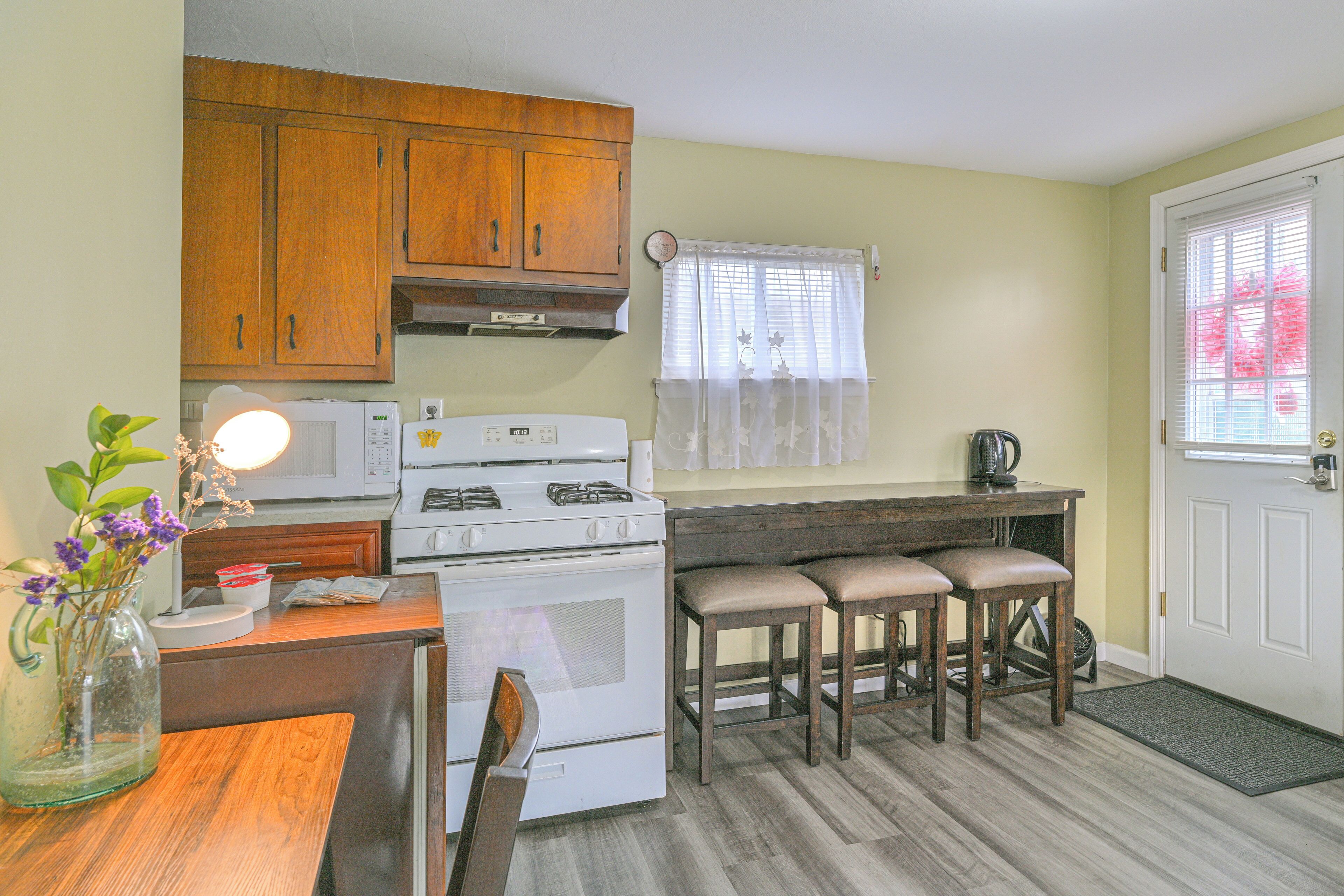 A kitchen with wooden cabinets, a white stove, a dining table with two chairs, and a window with a curtain.