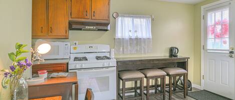 A kitchen with wooden cabinets, a white stove, a dining table with two chairs, and a window with a curtain.