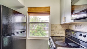 A kitchen with a black refrigerator, a stove, and a window with blinds. - Half-mi to Ocean: Cape Canaveral Beach Hideaway! (Cape Canaveral)