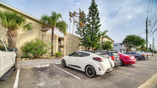 A parking lot with several cars, including a white sports car, parked in front of a building with a beige facade and a balcony. - Half-mi to Ocean: Cape Canaveral Beach Hideaway! (Cape Canaveral)