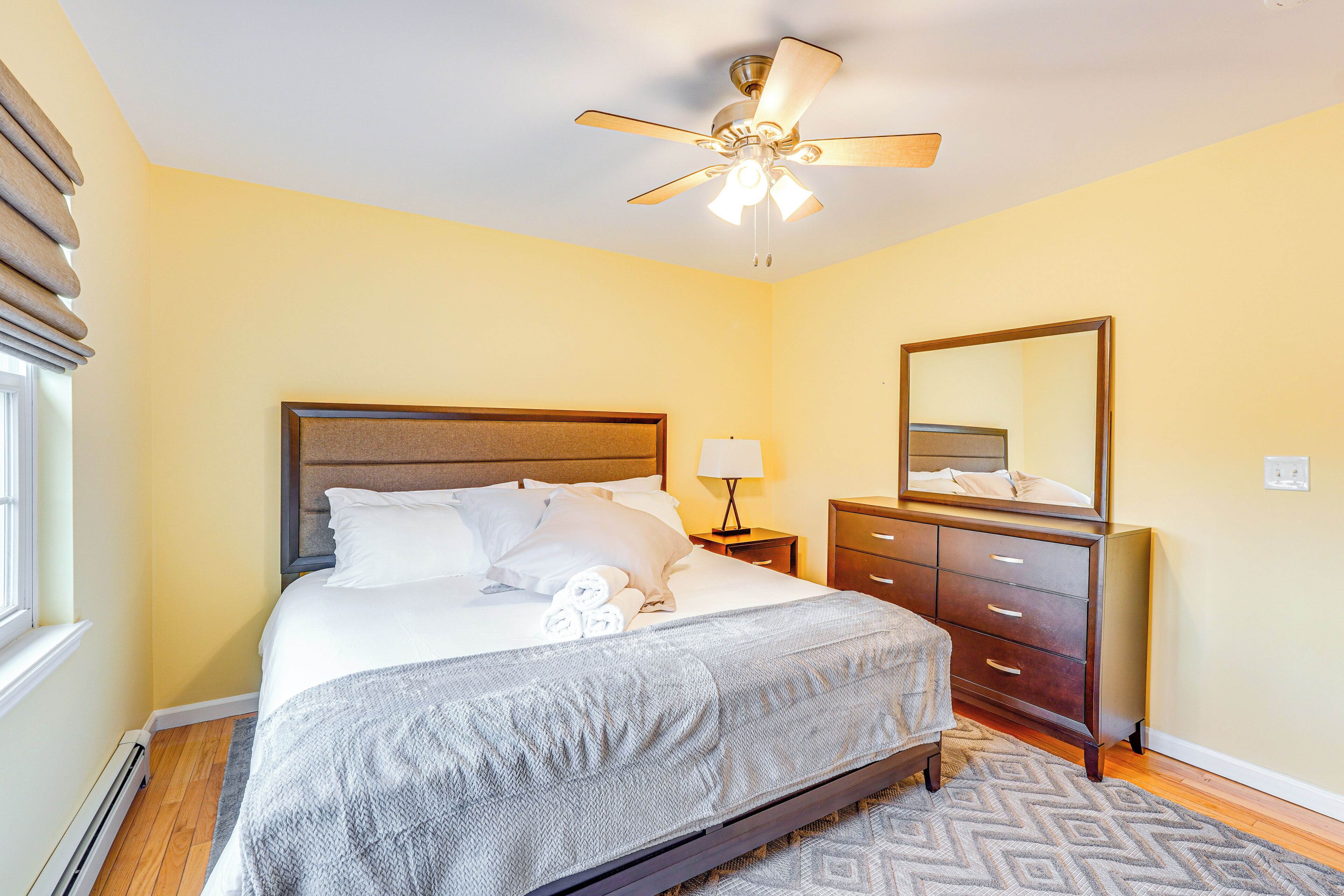 A bedroom with a bed, a nightstand, a dresser, a ceiling fan, and a window.