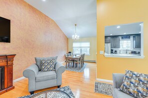A spacious living room with a fireplace, two grey sofas, a dining area, and a kitchen visible through an open door.