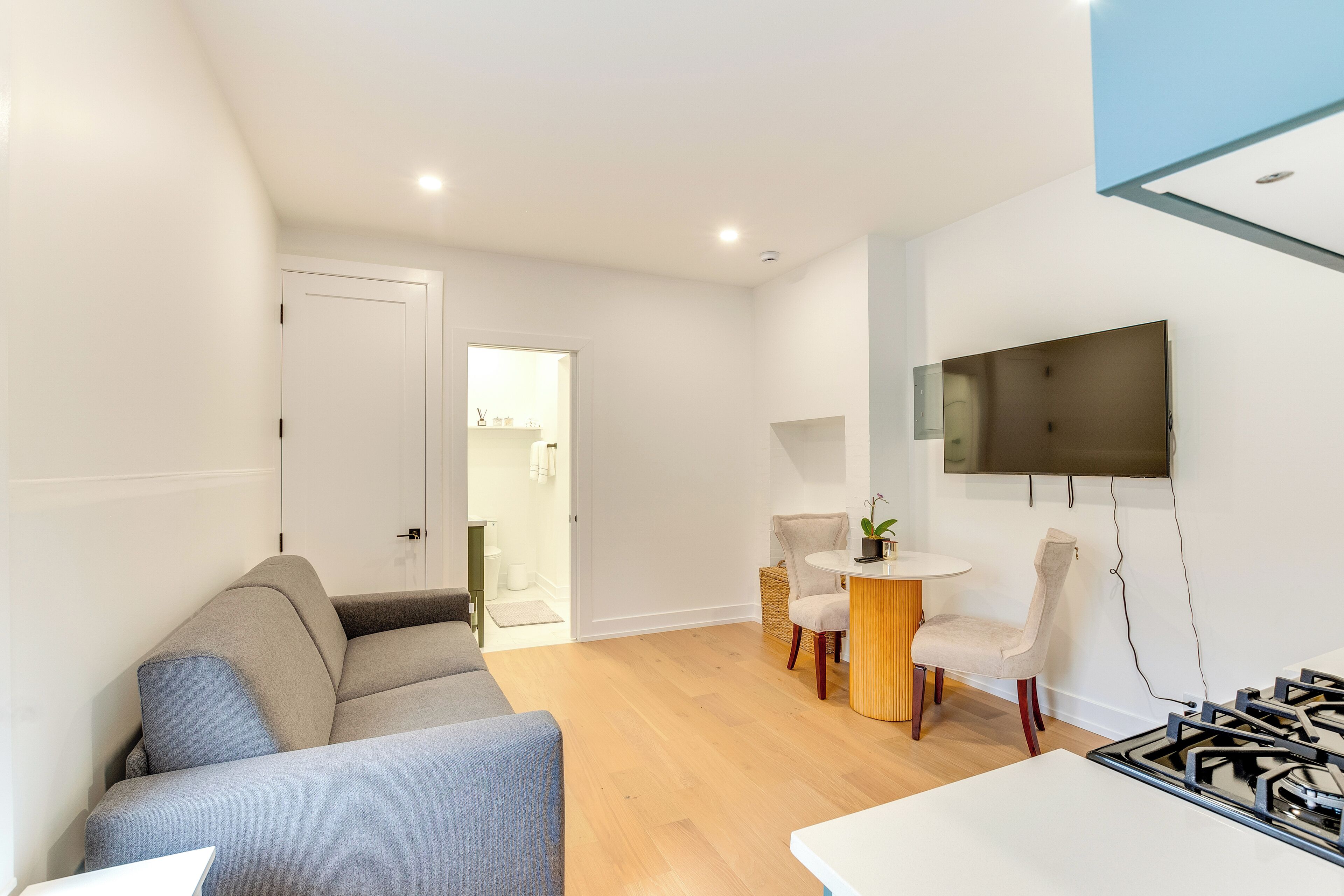 A modern living room with a grey sofa, a round wooden table, and a TV mounted on the wall.