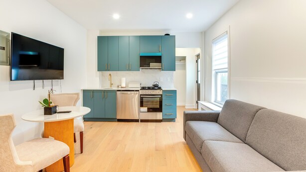 A modern kitchen with teal cabinets, a built-in oven, and a flat-screen TV mounted above the counter. - Centrally Located & Pet Friendly: Yonkers Studio! (Yonkers)