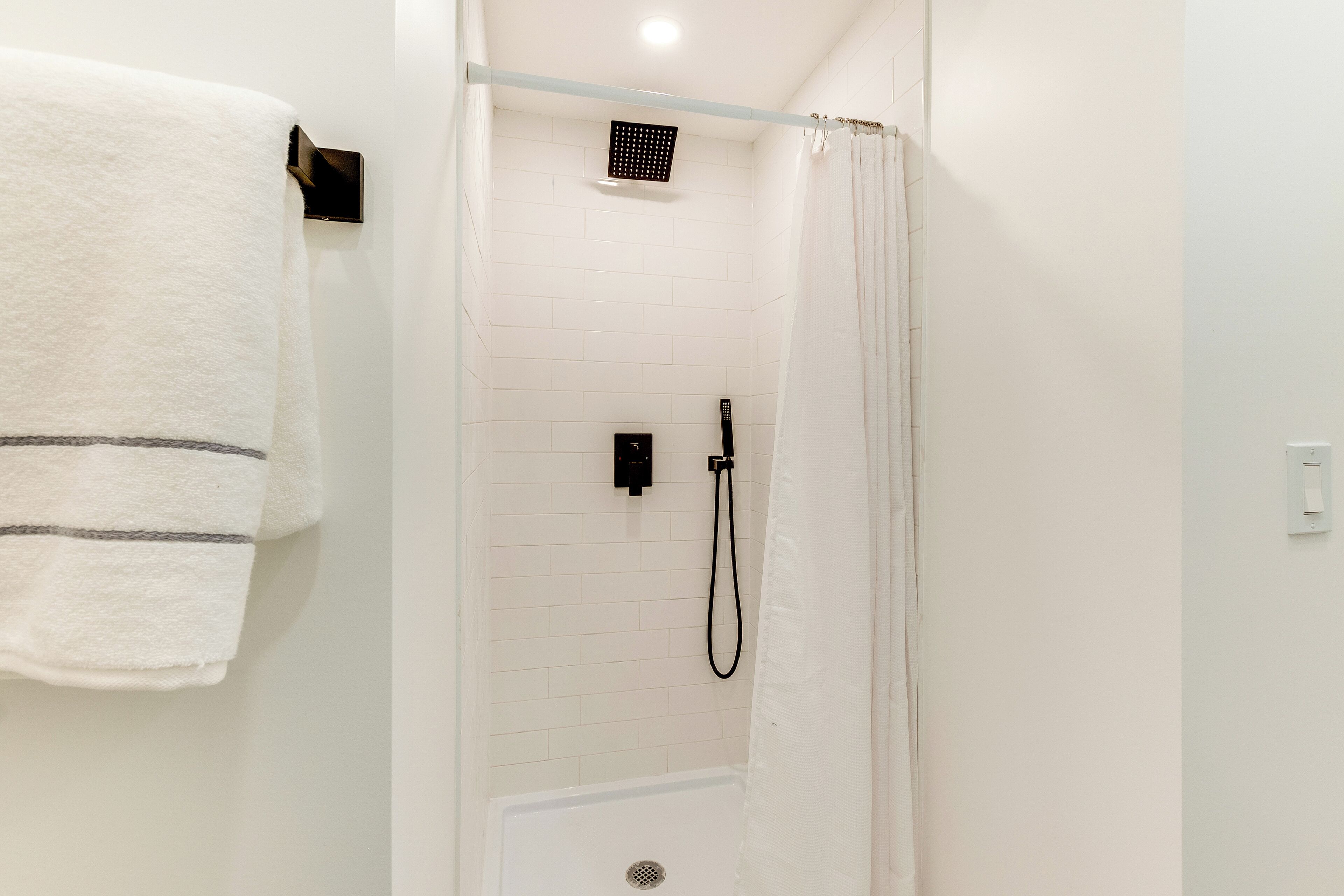 A shower area with a white tiled wall, a showerhead, and a handheld shower attachment.