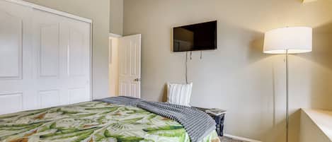 A bedroom with a bed, a television mounted on the wall, a floor lamp, and a door.
