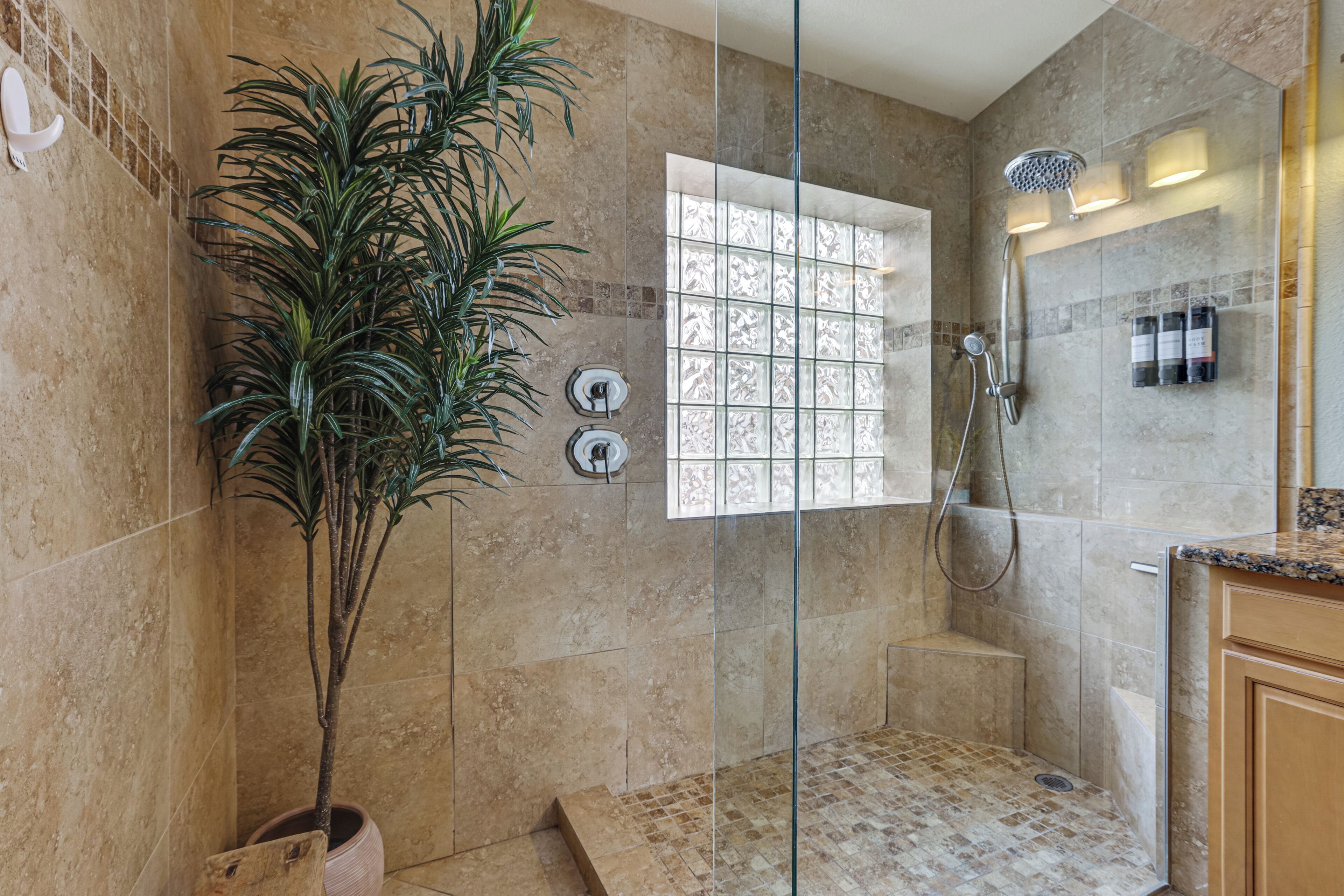 Une douche avec une porte en verre, une plante en pot et un sol carrelé.