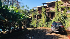 A rustic building with multiple balconies, surrounded by lush greenery and a cobblestone path.