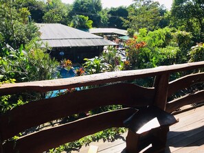 A wooden deck with a view of a building and lush greenery. - jasy hotel (Puerto Iguazú)