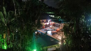 A nighttime view of a resort with a pool area, surrounded by dense tropical vegetation.