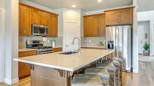 A modern kitchen with wooden cabinets, stainless steel appliances, a large island with bar stools, and a refrigerator. - Hike, Bike & Swim: Utah Family Home w/ Mtn Views! (Washington)