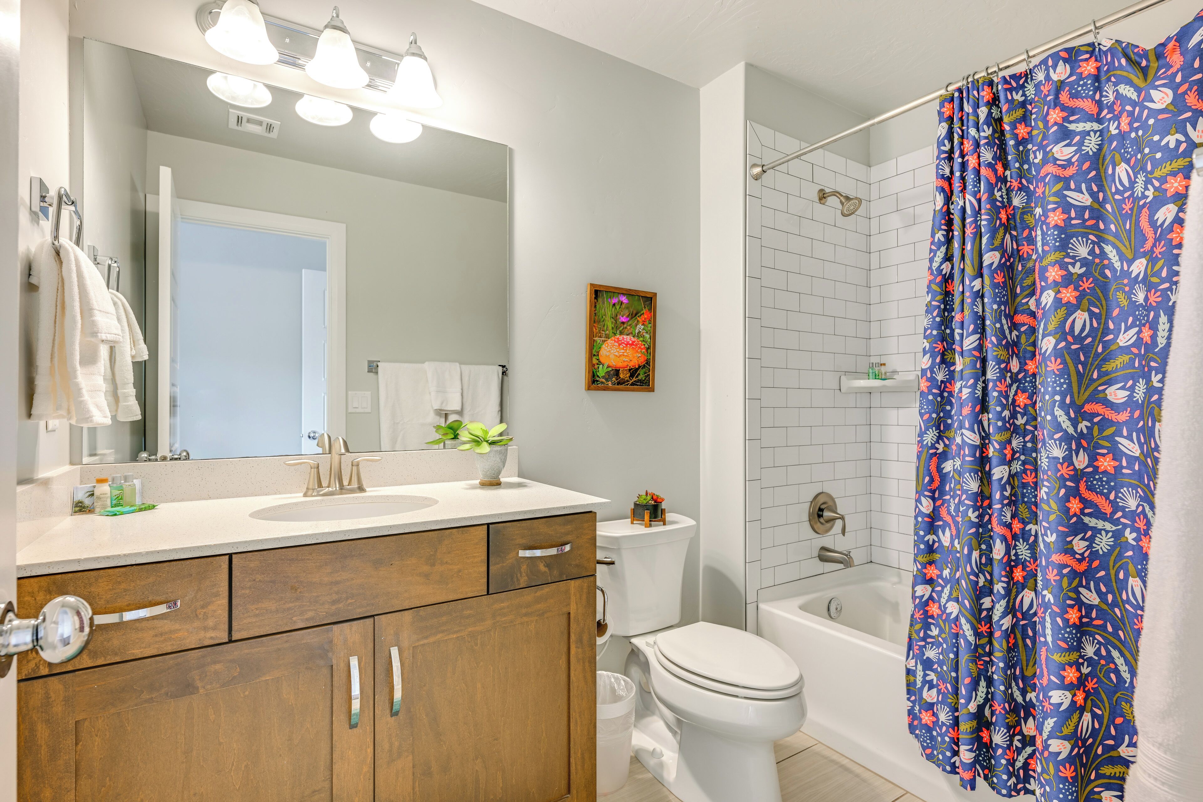 A bathroom with a wooden vanity, a white toilet, a bathtub, and a shower curtain with a floral pattern.