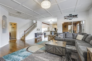 A spacious living room with a wooden staircase, a large sectional sofa, a coffee table, and a chandelier. - Pool & Spa: Spacious Port St Lucie Villa! (Port Saint Lucie)