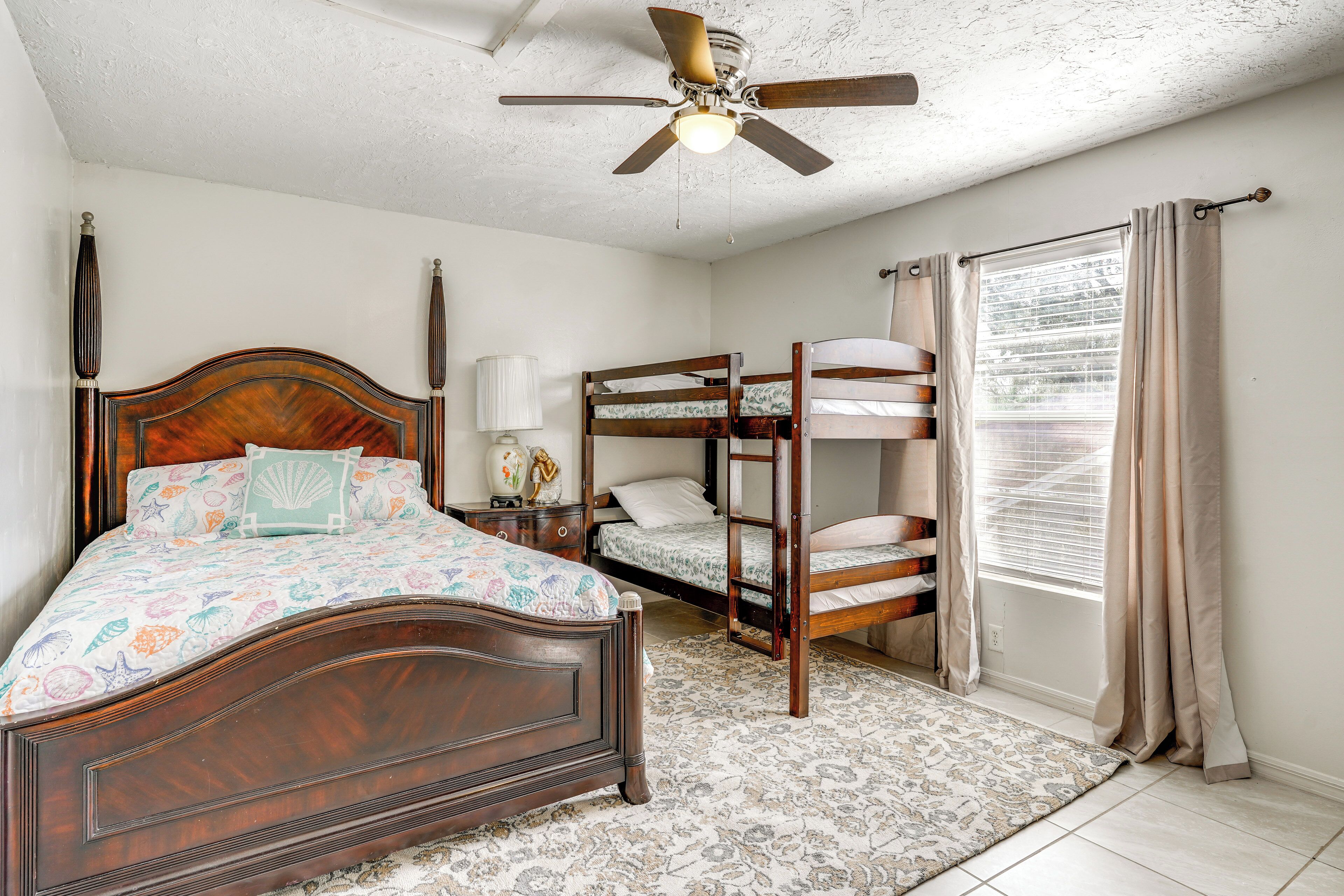 Une chambre avec un lit en bois, un lit superposé, un ventilateur de plafond, une fenêtre avec des rideaux et un tapis à motifs.