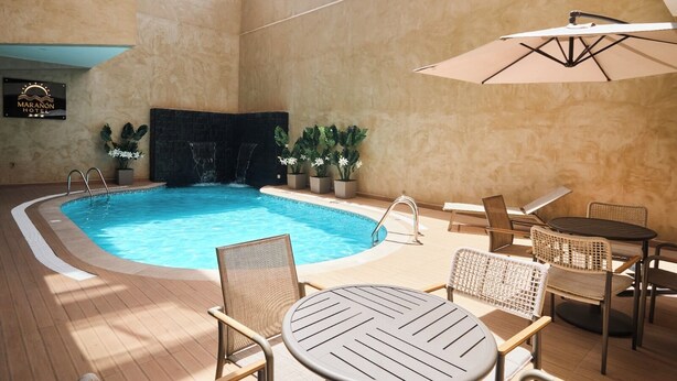 Une piscine intérieure agrémentée d’une cascade, entourée de chaises longues et de tables.
