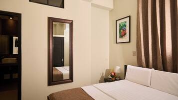 A hotel room with a bed, a bedside table with a lamp, a framed picture on the wall, and a window with curtains.