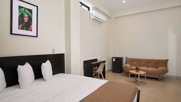 Habitación de hotel con cama, escritorio, sillón, sofá y una mesita con un florero.