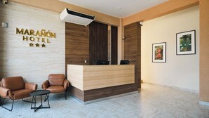 Un hall d’hôtel avec un comptoir d’accueil en bois, deux fauteuils en cuir et un sol en marbre.