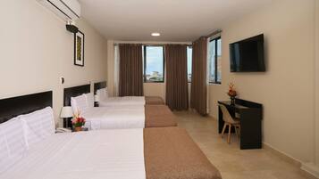 A hotel room with three beds, a desk, a TV, and a window with curtains.
