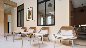 Un espace d’accueil avec des fauteuils en osier, une petite table ornée d’un vase de fleurs et un tableau encadré accroché au mur.