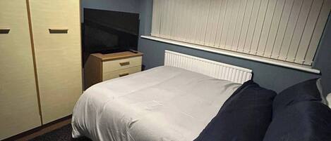 A bedroom with a bed, a dresser, a radiator, and a window with blinds.