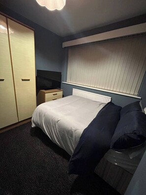 A bedroom with a bed, a dresser, a radiator, and a window with blinds. - Housesleeps9-fireplace-garden-bbq-tv (Manchester)