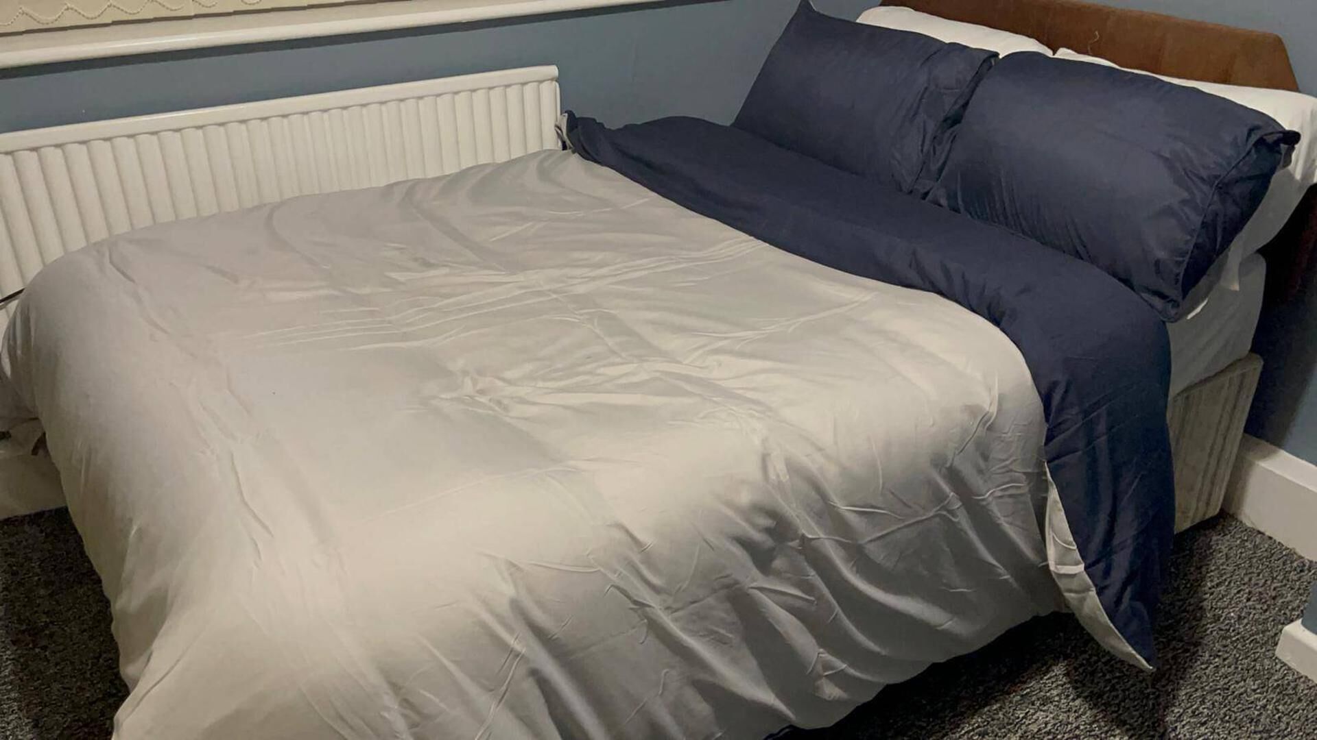 A bed with a white and blue duvet, a wooden headboard, and a white radiator.