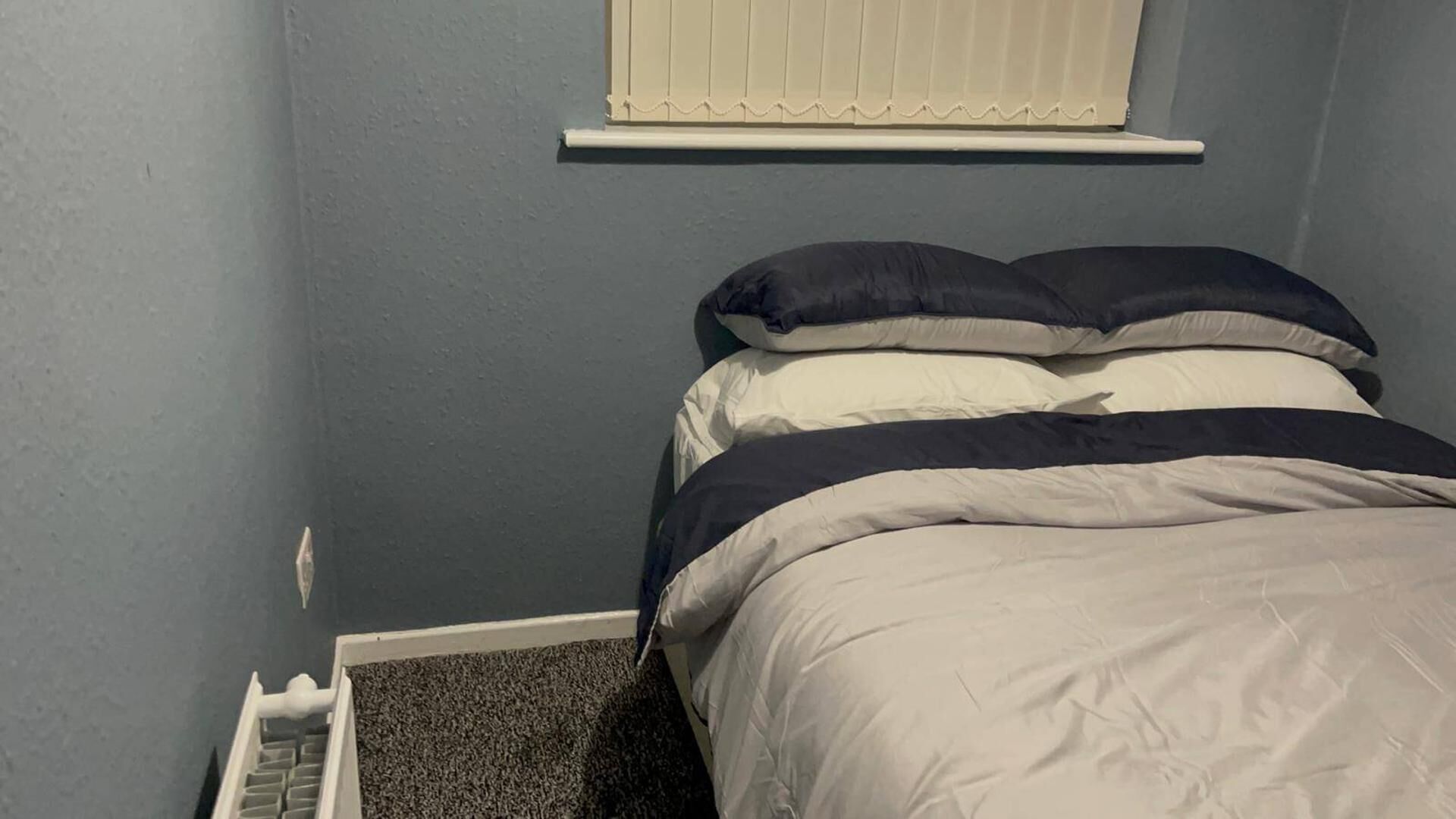 A bedroom with a bed, a window with blinds, and a radiator.