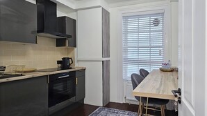 A compact kitchen with a built-in oven, a coffee maker, and a dining area with a table and chairs.