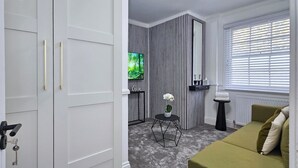 A modern living room with a grey sofa, a TV mounted on a striped wall, and a small side table with a plant.