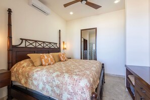 A bedroom with a bed, a ceiling fan, an air conditioning unit, and a mirror.