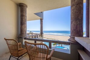 A balcony with wicker chairs, a pool, and a view of the beach. - Sol Pacifico Cerritos Deluxe Oceanfront Condo (Los Cerritos)
