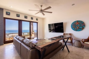 A living room with a large window, a ceiling fan, a flat-screen TV, and a starfish wall art piece.
