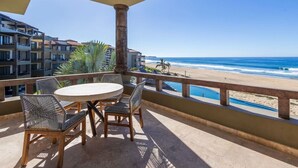 Varanda com mesa e cadeiras redondas, com vista para a praia e o oceano.
