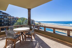 Ein Balkon mit einem runden Tisch und Stühlen, der Blick auf einen Strand und das Meer gewährt.