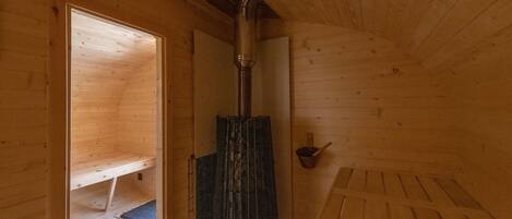 A wooden sauna room with a central heating column, a bench, and a small shelf.