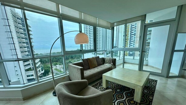 A modern living room with a sofa, armchair, and coffee table, large windows offering a city view. - River Wood I Sunny 1 BDR in Costa del Este (Panama City)