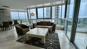 A spacious living room with a large window, a sofa, a coffee table, and a dining area. - River Wood I Sunny 1 BDR in Costa del Este (Panama City)
