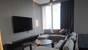 A modern living room with a flat-screen TV mounted on the wall, a sectional sofa, a coffee table, and a side table.