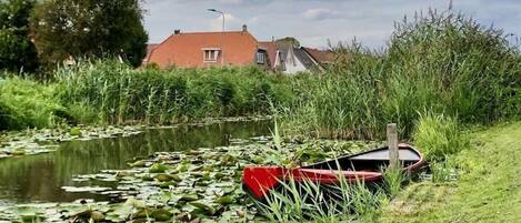 A calm pond with lily pads and a red boat on the grass beside it.